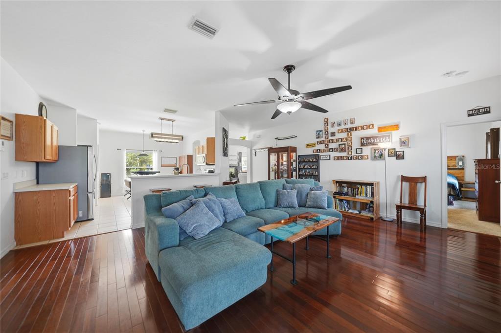 A living room with a blue sectional sofa, hardwood floors, and an open kitchen — 4481 BALSEY STREET, NORTH PORT, FL
