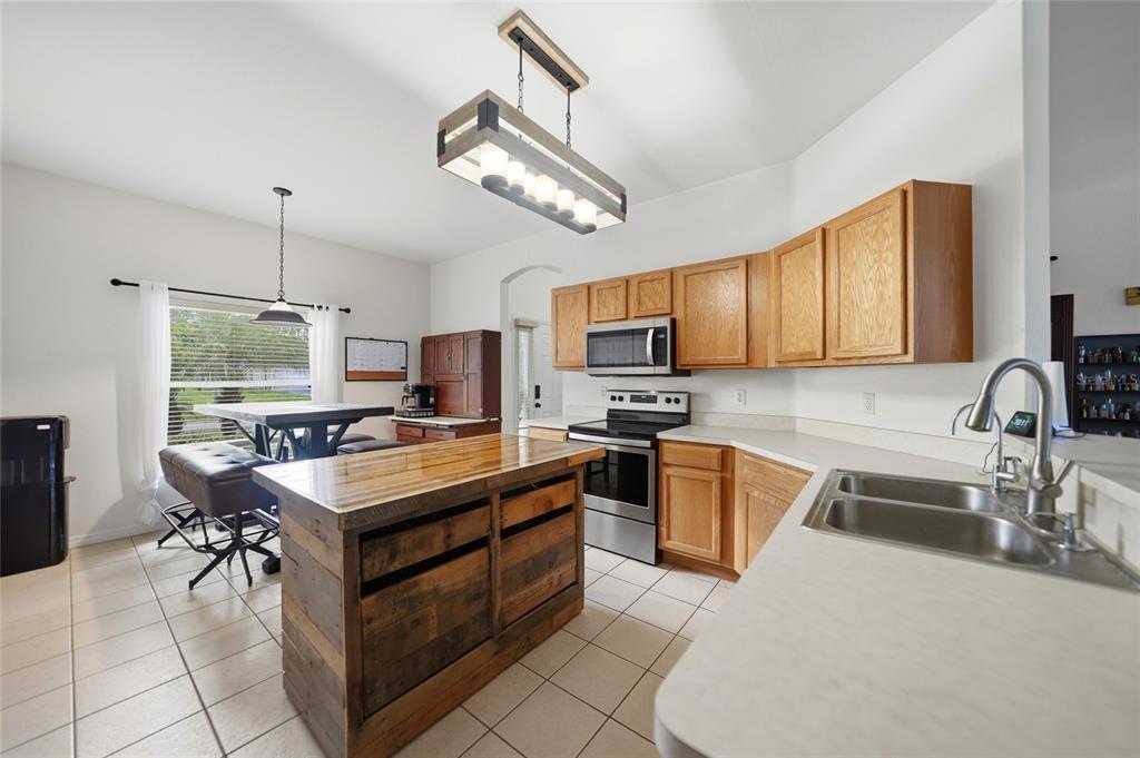 A kitchen features wood cabinets, a rustic wooden island, stainless steel appliances, and tile flooring — 4481 BALSEY STREET, NORTH PORT, FL