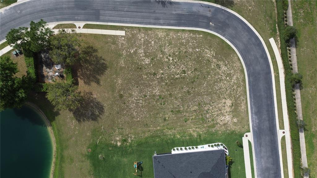 An aerial view shows a vacant corner residential lot bordered by a curved road — 760 WATER FERN TRAIL DRIVE, AUBURNDALE, FL