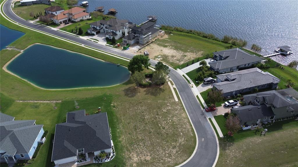 An aerial view shows a suburban neighborhood with houses, a lake, and a vacant lot — 760 WATER FERN TRAIL DRIVE, AUBURNDALE, FL