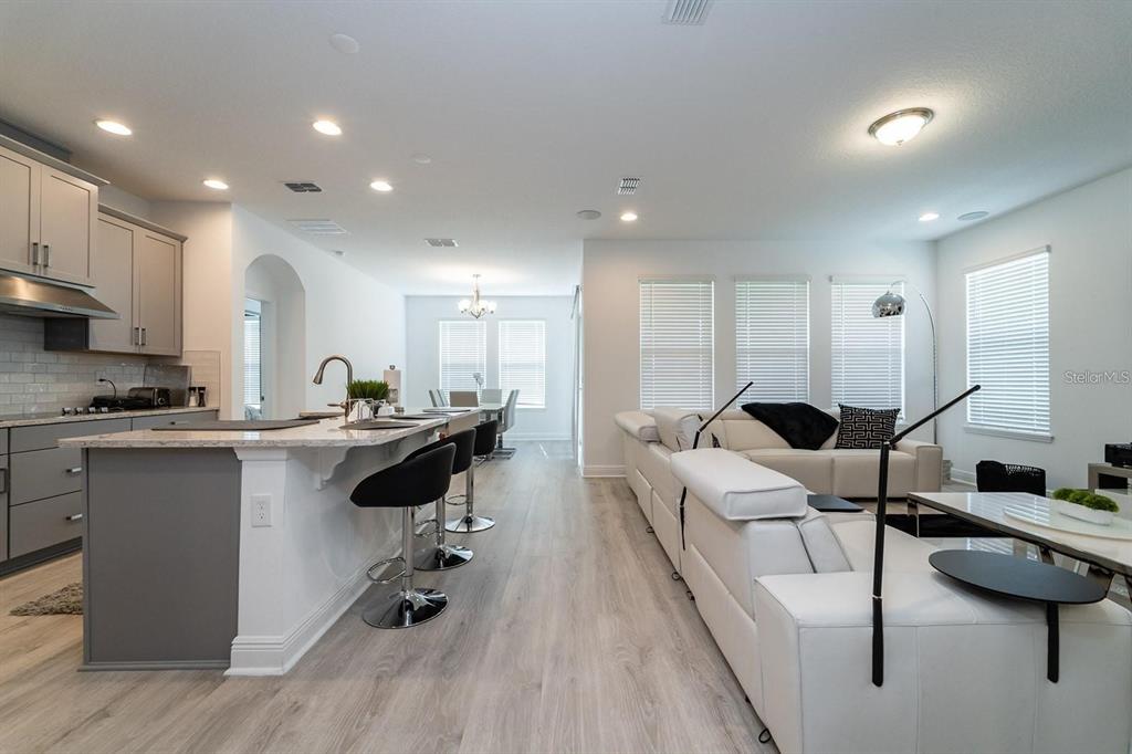 An open-concept kitchen and living area features light wood flooring, white cabinetry, and white furniture — 9296 BOLERO ROAD, WINTER GARDEN, FL