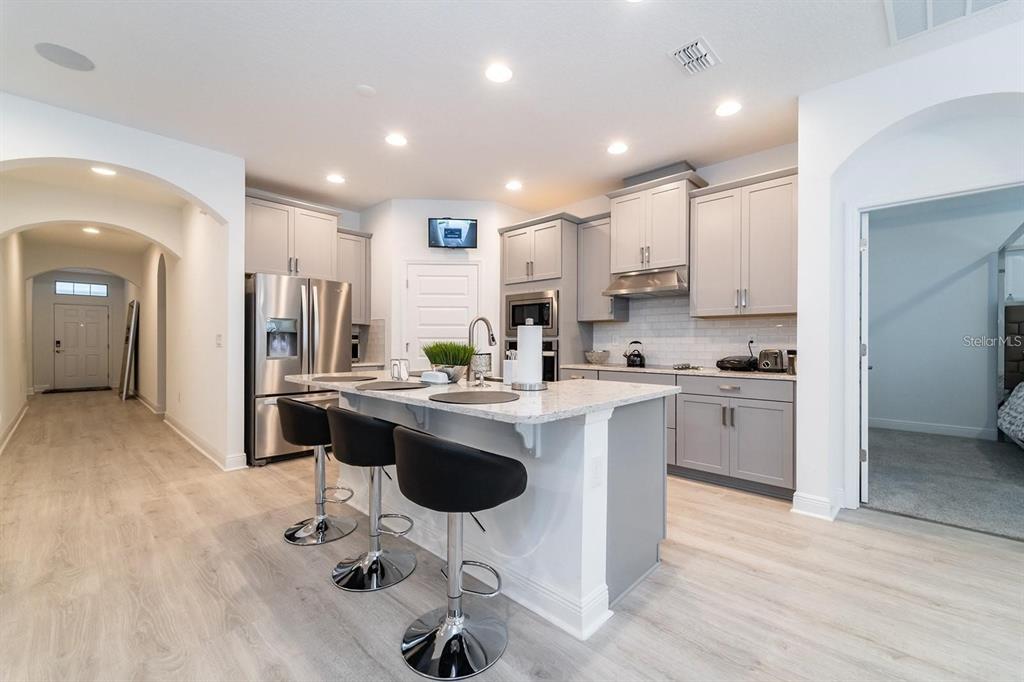 A modern kitchen features gray cabinets, granite countertops, a central island, and stainless steel appliances — 9296 BOLERO ROAD, WINTER GARDEN, FL