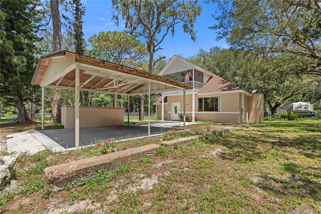 A tan two-story house features a large metal carport and a second-story balcony with flag — 7803 CADILLAC AVENUE, HUDSON, FL