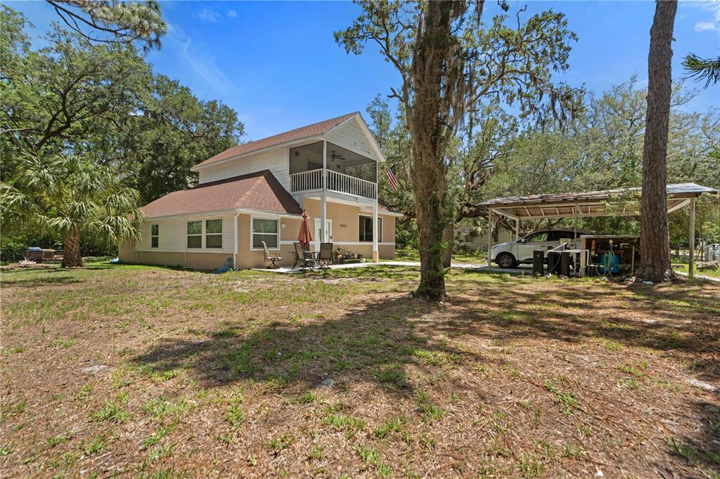 A two-story house with a screened balcony, a brown roof, and an adjacent metal carport — 7803 CADILLAC AVENUE, HUDSON, FL