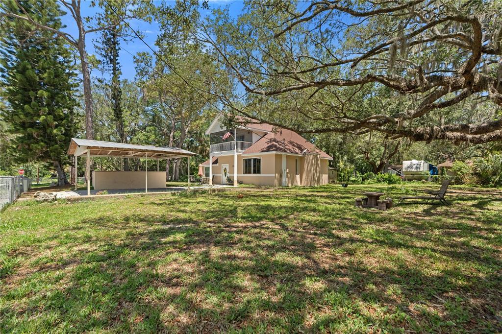 A two-story house with a detached carport sits on a large, tree-shaded grassy lot — 7803 CADILLAC AVENUE, HUDSON, FL