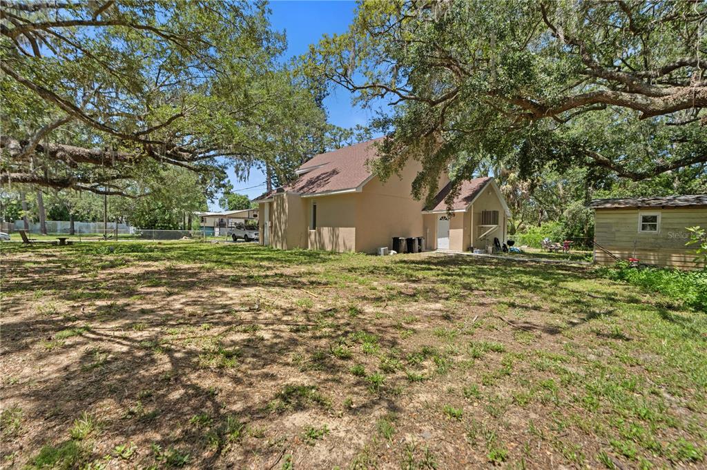 A tan house with a brown roof sits on a large, tree-shaded grassy lot — 7803 CADILLAC AVENUE, HUDSON, FL