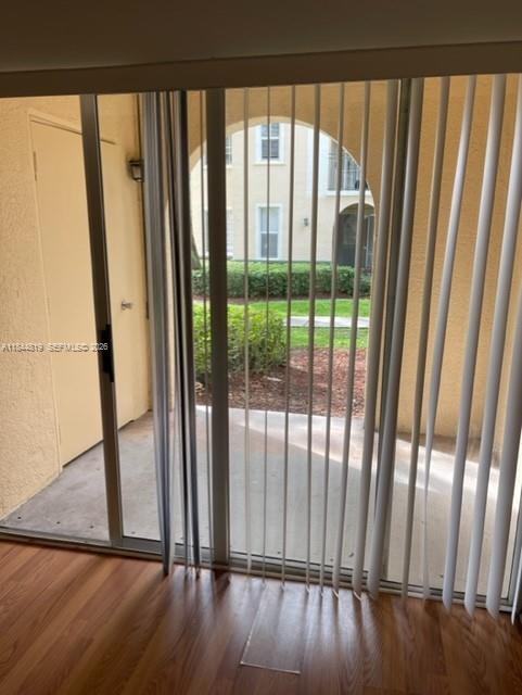 A view from inside through a sliding glass door with vertical blinds onto a concrete patio — 2494 Centergate Dr # 102, Miramar FL 33025, MIRAMAR, FL