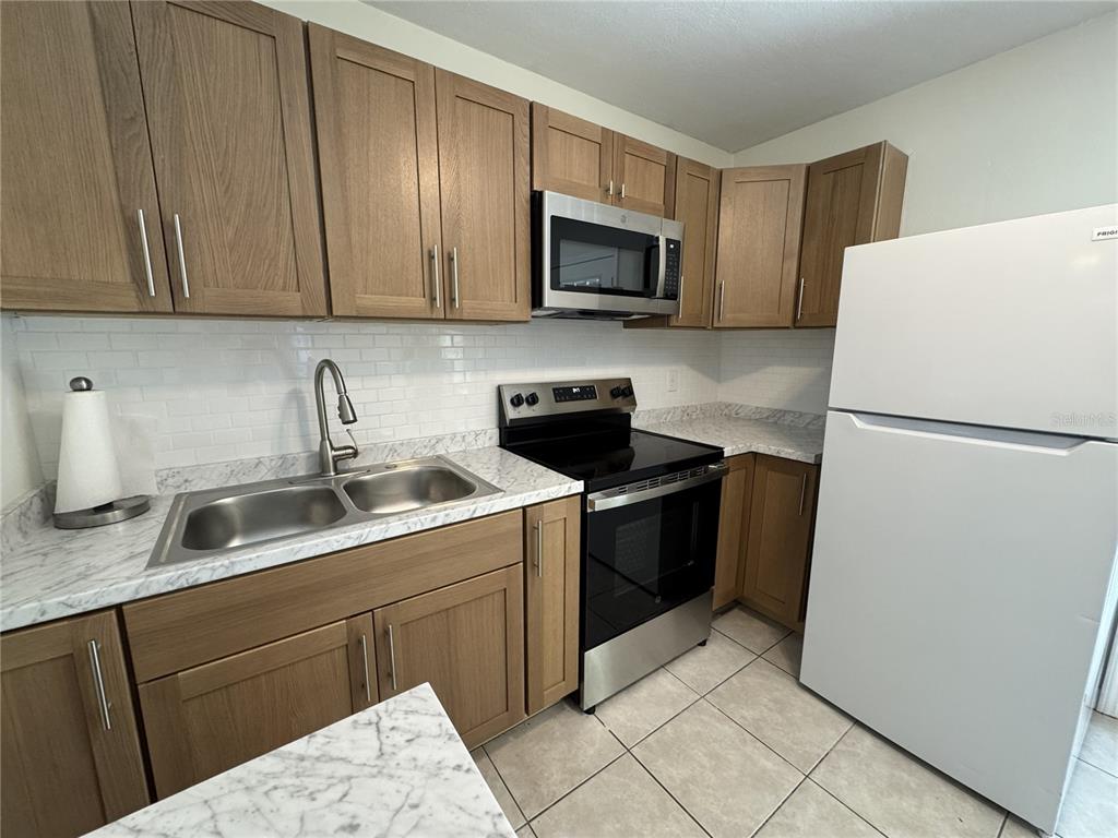 A kitchen features light wood cabinets, marble-patterned countertops, stainless steel appliances, and white subway tile — 516 LAUREL ROAD W, NOKOMIS, FL