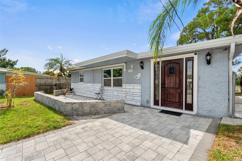 A light blue house exterior features a stone-paved patio, a low wall, and a wooden door — 7235 MARYLAND AVENUE, HUDSON, FL