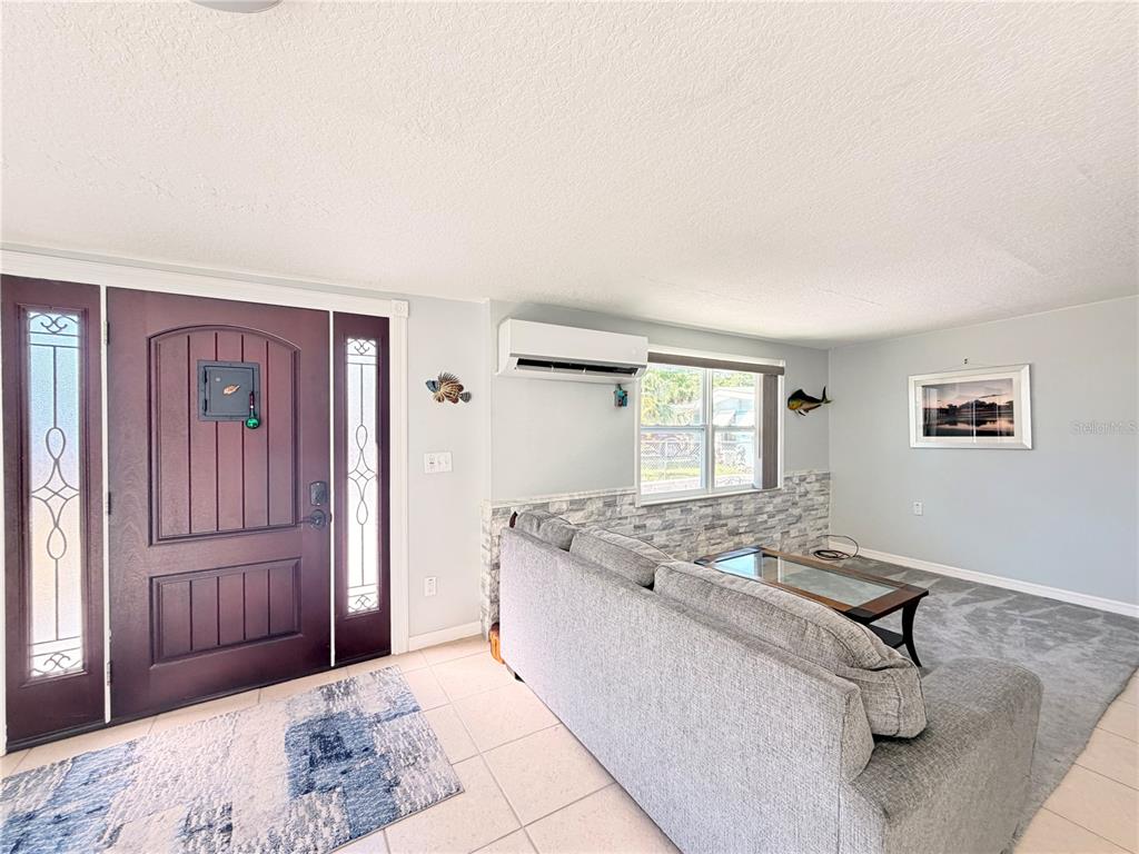 A living room features a dark front door, a gray sofa, and a wall-mounted air conditioner — 7235 MARYLAND AVENUE, HUDSON, FL