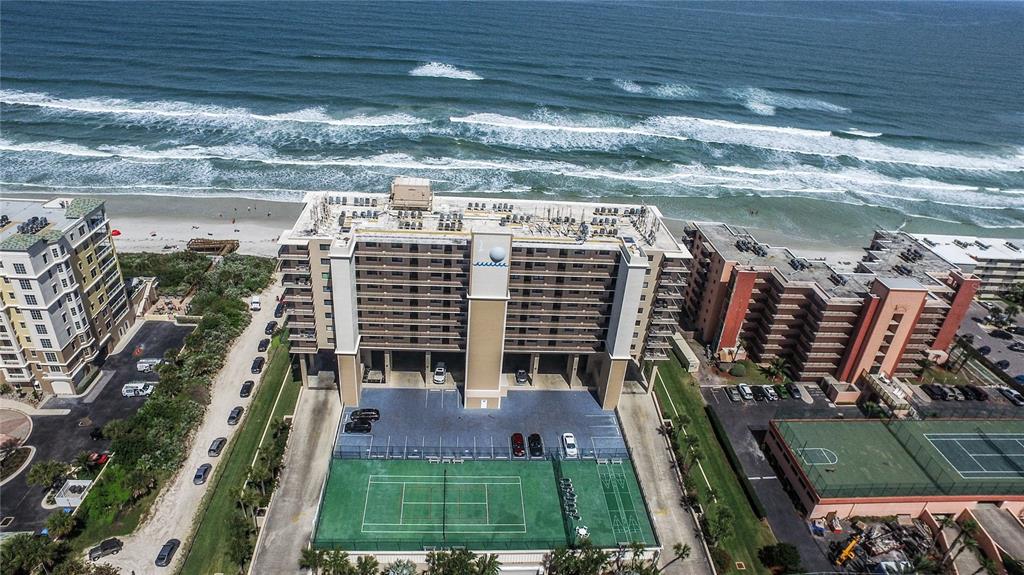 An aerial view shows a beachfront condominium building with a tennis court and parking lot — 4139 ATLANTIC UNIT A406, NEW SMYRNA BEACH, FL