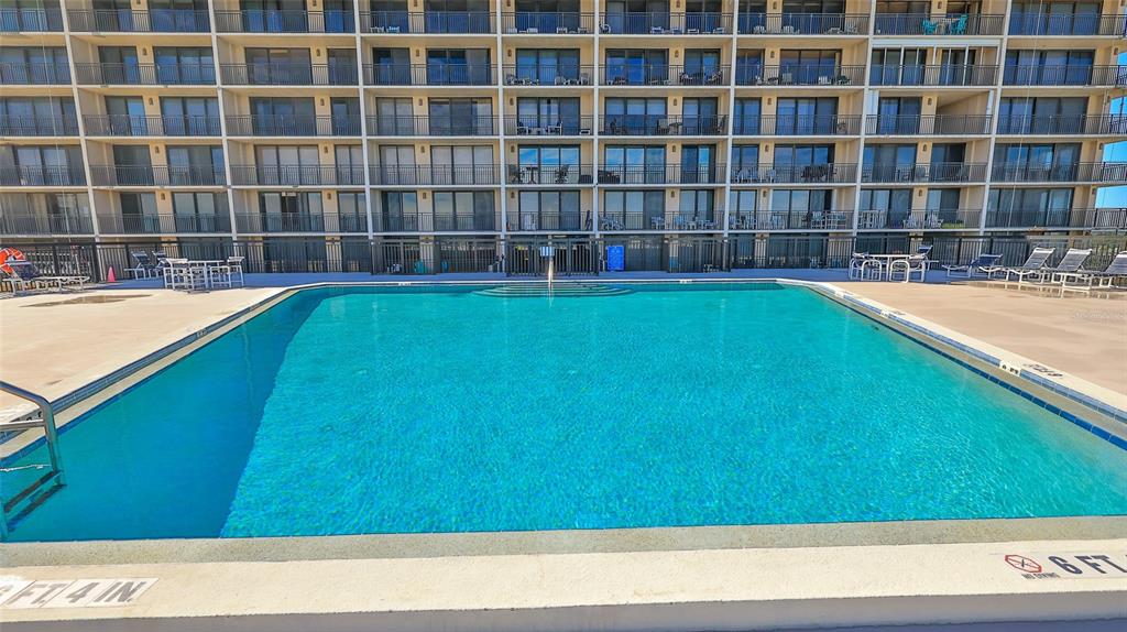 A large rectangular swimming pool sits on a concrete deck in front of a building — 4139 ATLANTIC UNIT A406, NEW SMYRNA BEACH, FL