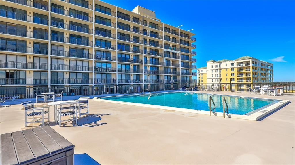 A swimming pool sits on a patio deck in front of a large multi-story building — 4139 ATLANTIC UNIT A406, NEW SMYRNA BEACH, FL