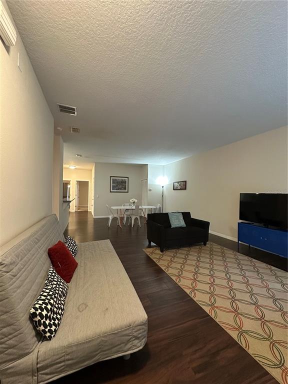 A living room with dark wood floors, a sofa, a black armchair, and a dining area — 3123 SUN LAKE COURT UNIT A, KISSIMMEE, FL