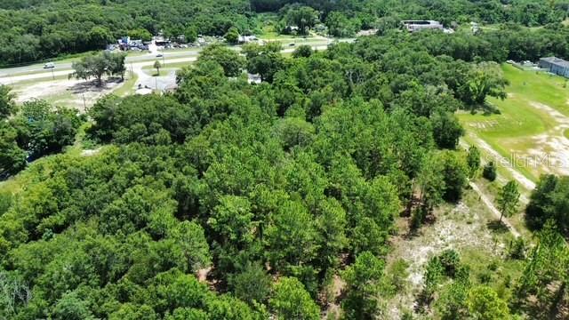 An aerial view shows a dense, wooded lot adjacent to a paved road and open fields — 4026 N ORANGE BLOSSOM TRAIL, MOUNT DORA, FL