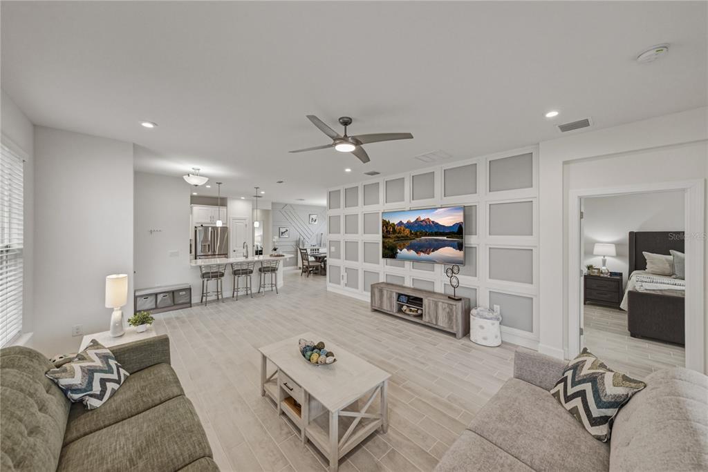 A living room with light wood-look tile floors, a paneled accent wall, and an open kitchen — 4248 CAIROLI COURT, WESLEY CHAPEL, FL