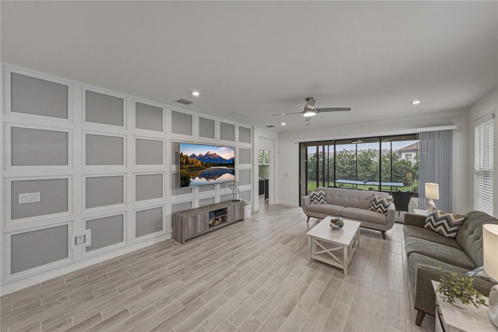 A living room features a grid-paneled accent wall, a wall-mounted television, and wood-look tile flooring — 4248 CAIROLI COURT, WESLEY CHAPEL, FL