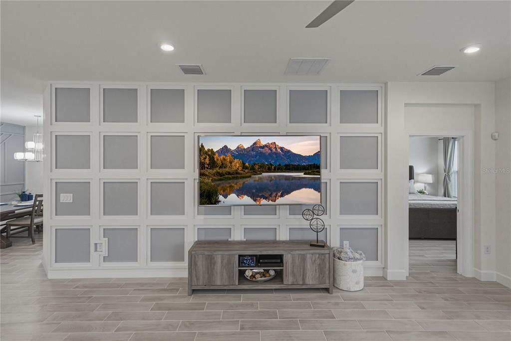 A living room features a grid-paneled accent wall with a mounted television and wood console — 4248 CAIROLI COURT, WESLEY CHAPEL, FL