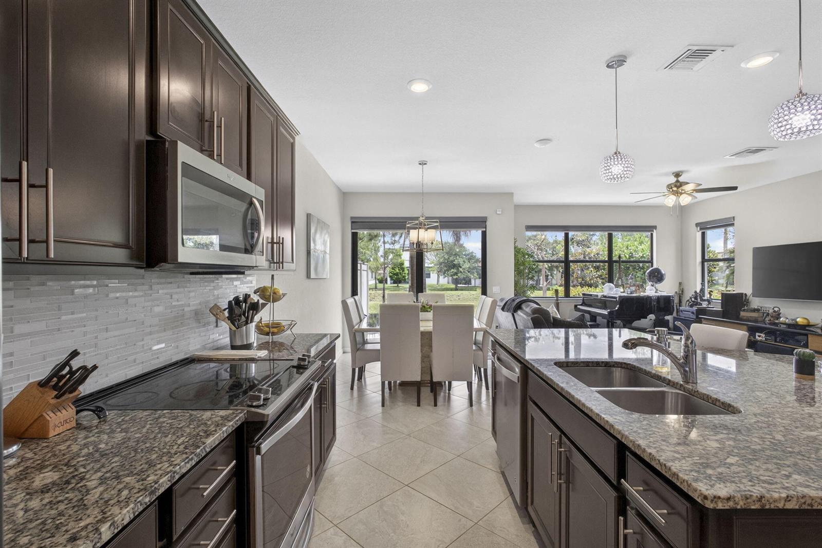 A kitchen with dark cabinets and granite countertops overlooks a dining area and living room — 8347 Cadre Noir Road, Lake Worth FL 33467, LAKE WORTH, FL
