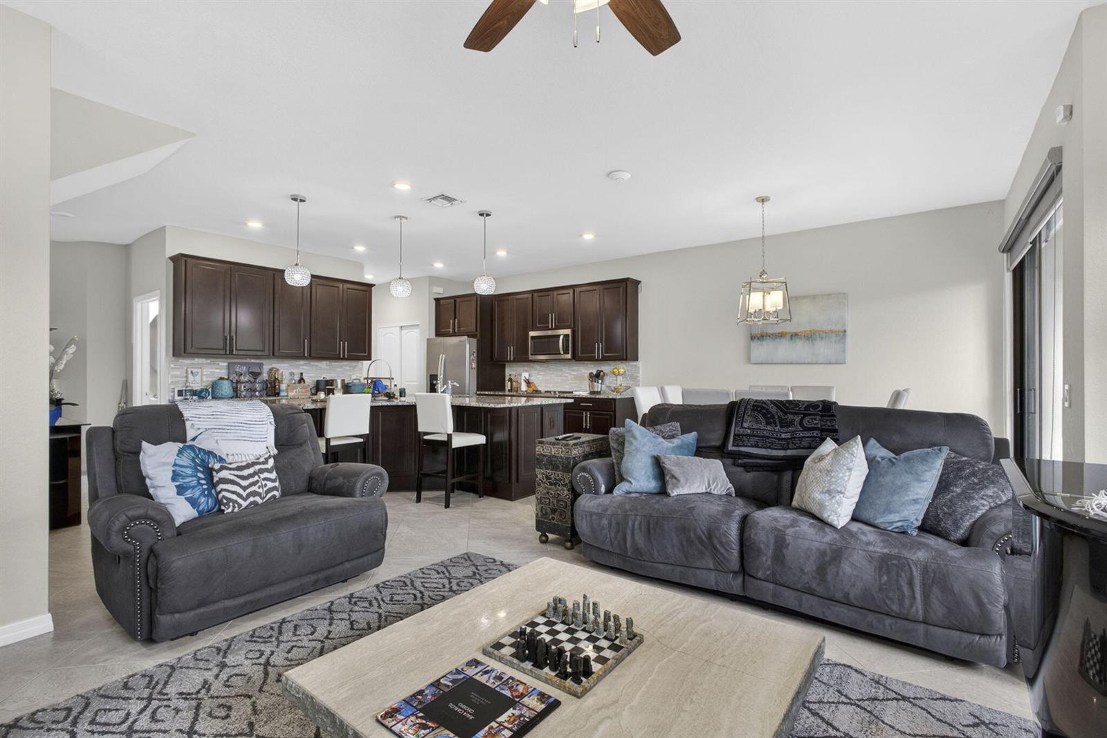 A living room with gray sofas and a coffee table opens into a dark-wood kitchen — 8347 Cadre Noir Road, Lake Worth FL 33467, LAKE WORTH, FL