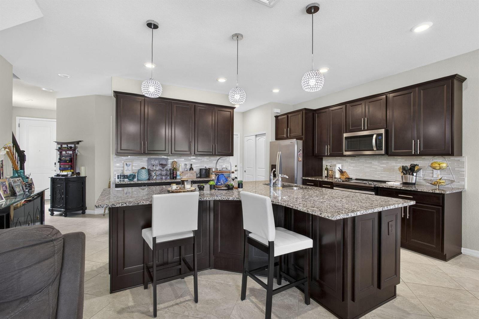 A kitchen with dark wood cabinets, granite countertops, an island, and three pendant lights — 8347 Cadre Noir Road, Lake Worth FL 33467, LAKE WORTH, FL