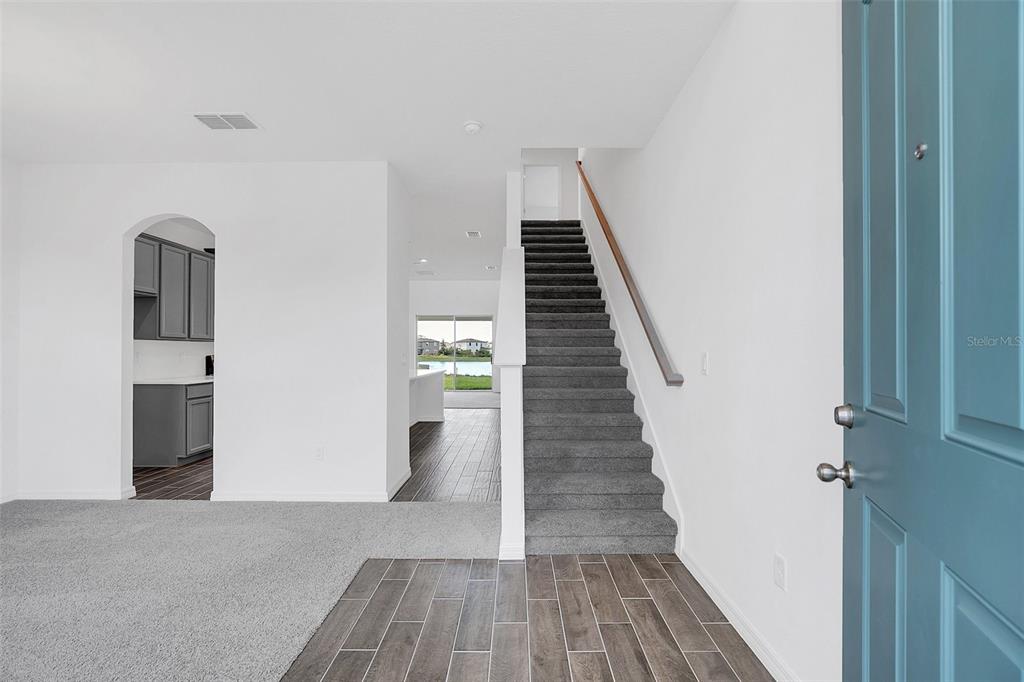 An entryway features a blue door, gray carpeted stairs, and wood-look tile flooring — 1217 GRASSLAND AVENUE, ST CLOUD, FL