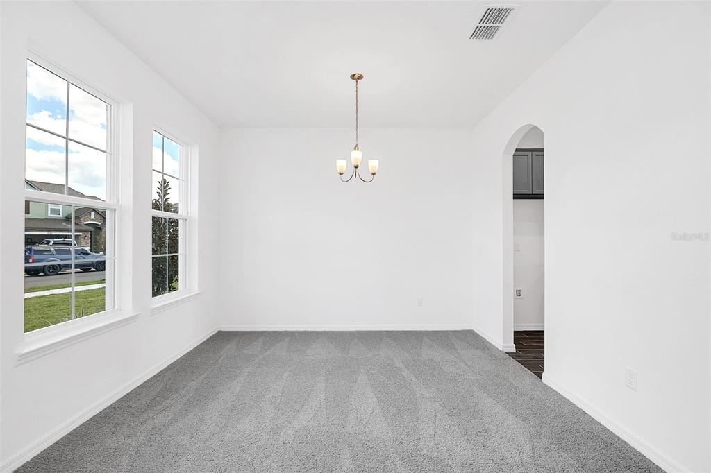A dining room with gray carpet, white walls, a chandelier, and two windows — 1217 GRASSLAND AVENUE, ST CLOUD, FL