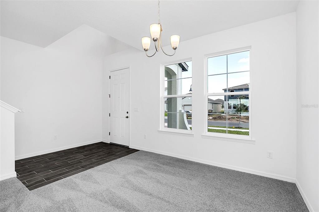 A room with gray carpet, a dark wood-look entryway, two windows, and a chandelier — 1217 GRASSLAND AVENUE, ST CLOUD, FL