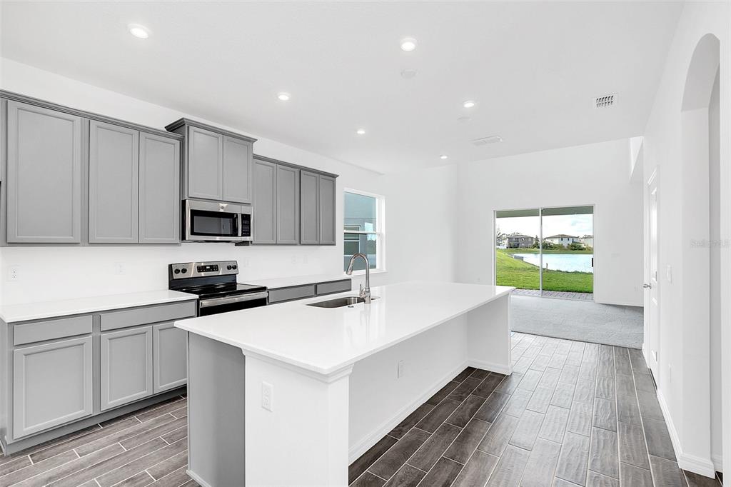 A modern kitchen features gray cabinets, a white island, and tile flooring overlooking a lake — 1217 GRASSLAND AVENUE, ST CLOUD, FL