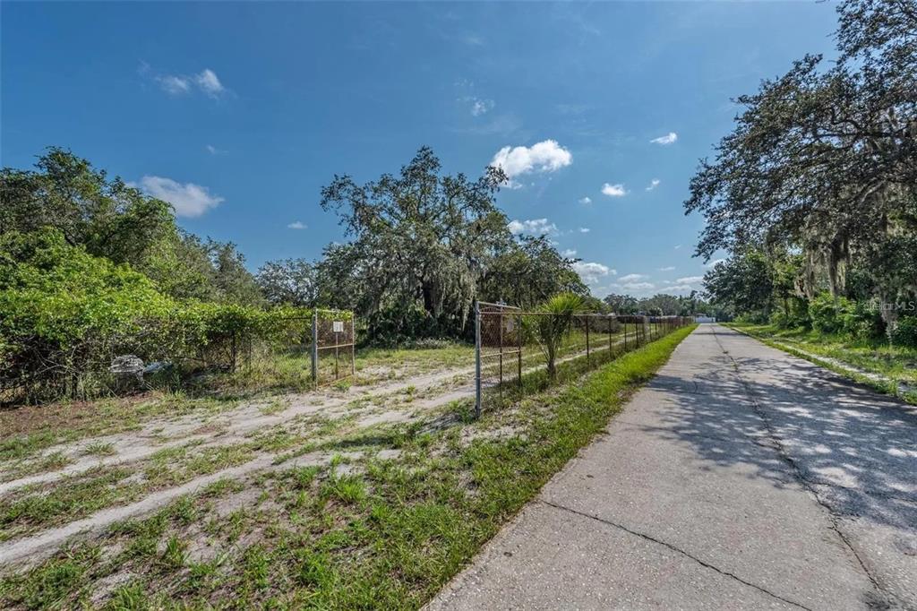 A dirt driveway leads through a chain-link gate into a wooded lot beside a road — 12154 BULLFROG CREEK ROAD, GIBSONTON, FL