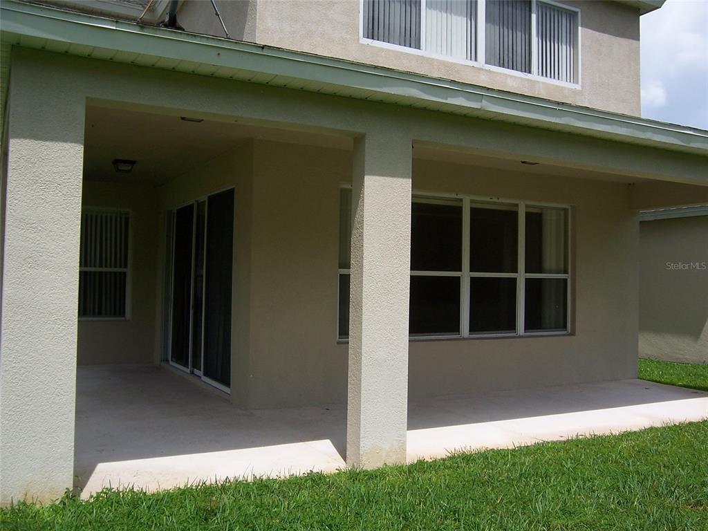 A covered concrete patio sits beneath the second story of a beige stucco house — 8631 GREENBANK BOULEVARD, WINDERMERE, FL