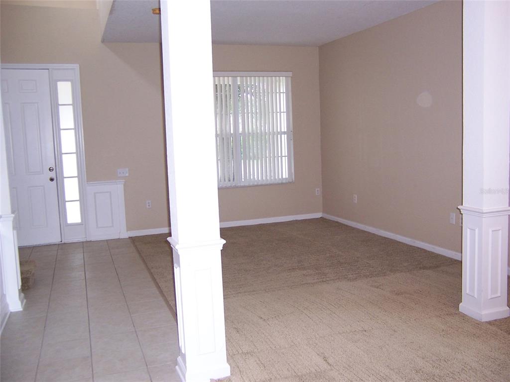 An empty living room features beige carpet, tan walls, and two white decorative columns — 8631 GREENBANK BOULEVARD, WINDERMERE, FL