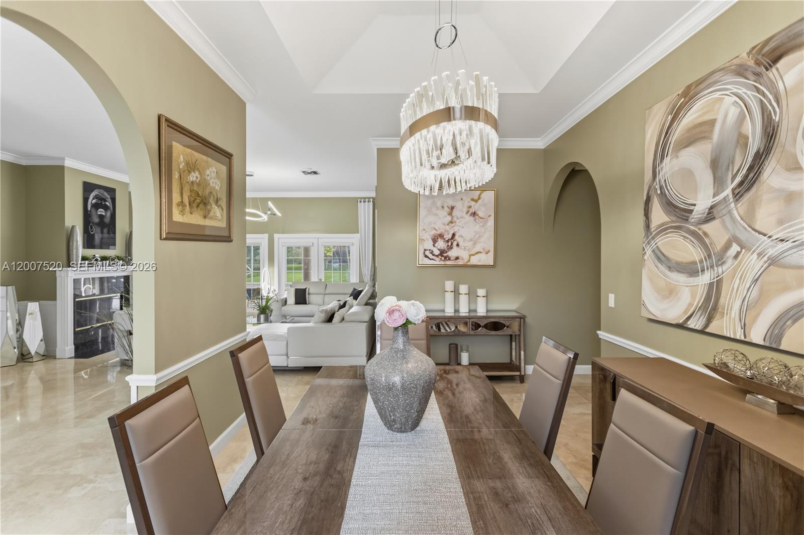 A dining room features a wood table, modern chandelier, and an arched entryway to the living room — 12343 NW 19th St, Plantation FL 33323, PLANTATION, FL