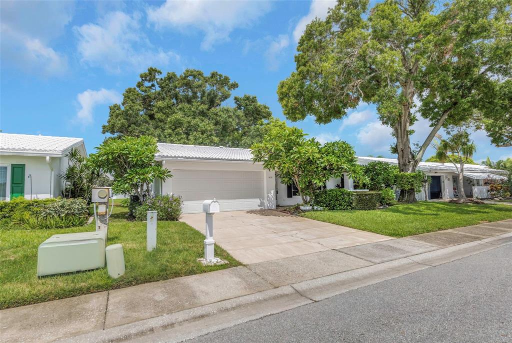 A white single-story house with a garage, concrete driveway, and large trees in the yard — 9110 40TH WAY N, PINELLAS PARK, FL