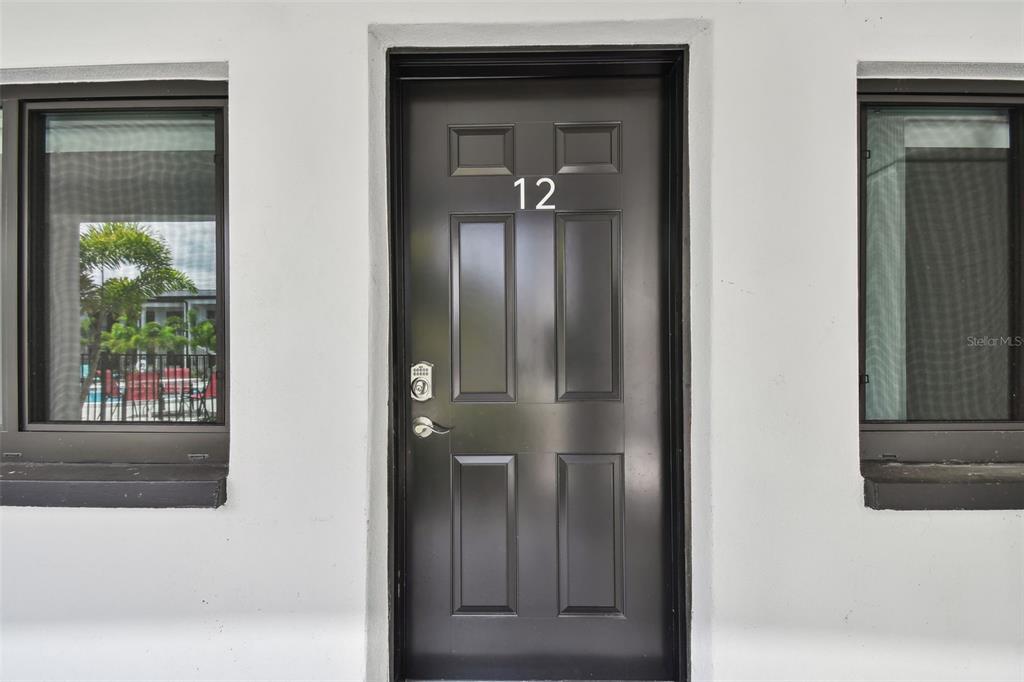 A black front door with the number 12 is centered between two windows on a wall — 2942 W BAY DRIVE UNIT 22, BELLEAIR BLUFFS, FL