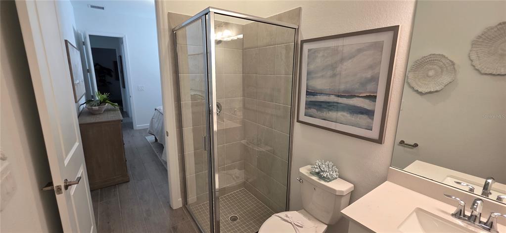 A bathroom features a glass-enclosed shower, a toilet, a vanity, and wood-look tile flooring — 8006 LAKES EDGE LANE, PORT CHARLOTTE, FL