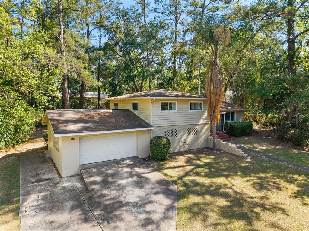 An exterior view of a two-story house with a garage, light siding, and surrounding trees — 2910 SW 1ST AVENUE, GAINESVILLE, FL