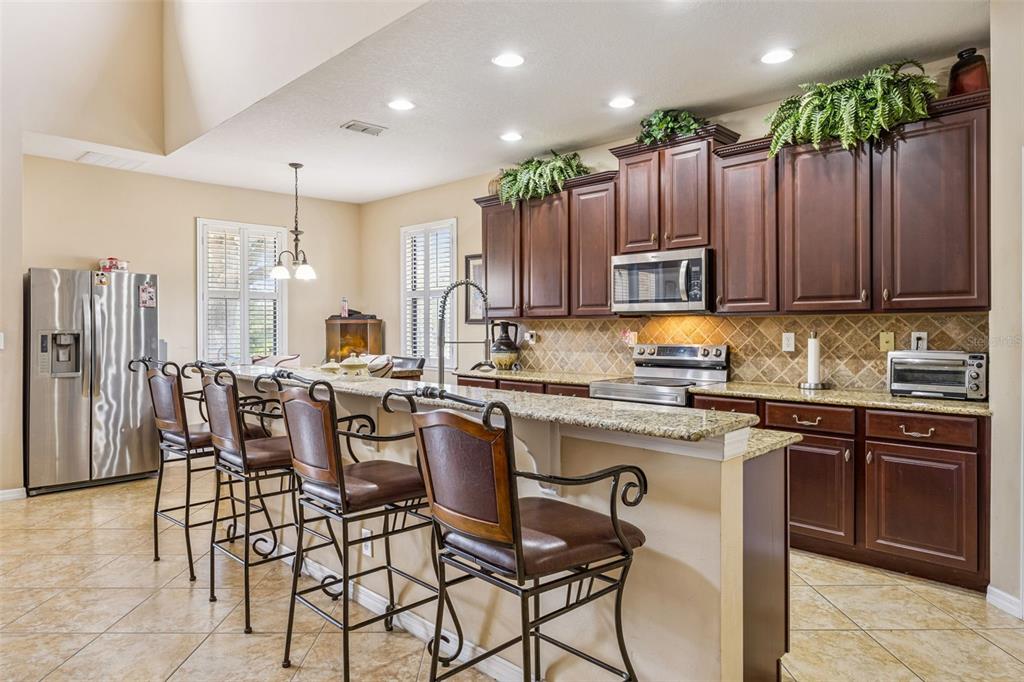 A kitchen features dark wood cabinets, granite countertops, a breakfast bar, and tile flooring — 3676 BRIAR RUN DRIVE, CLERMONT, FL