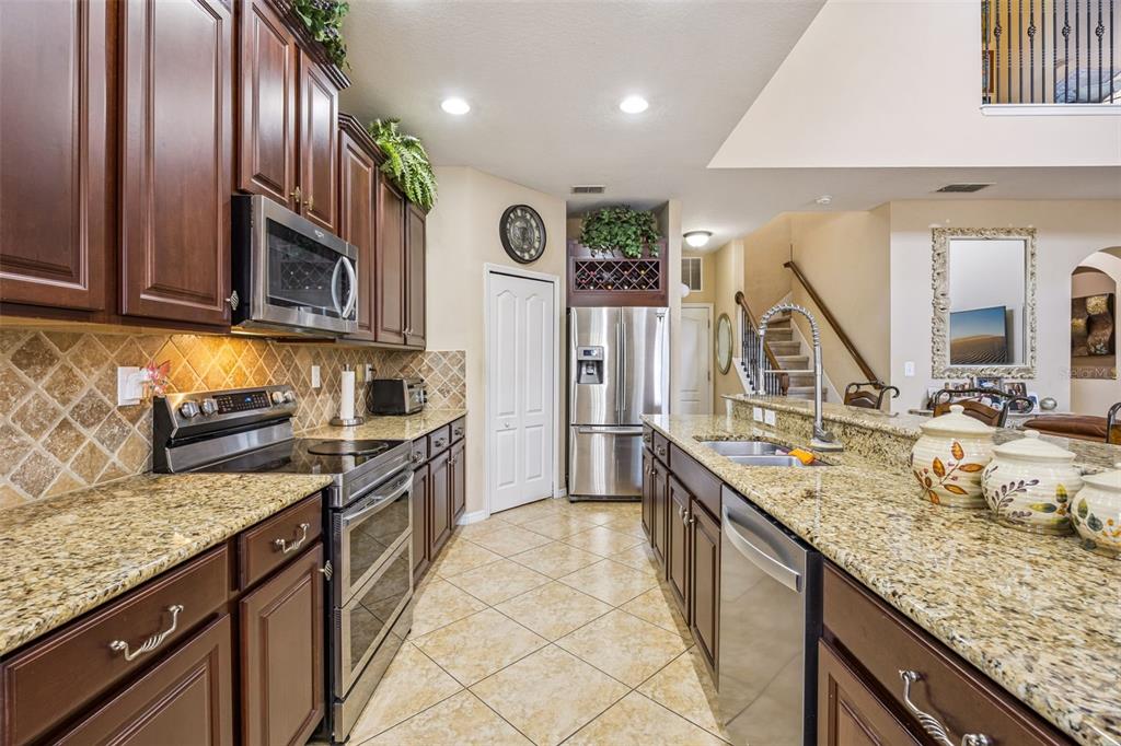 A kitchen with dark wood cabinets, granite countertops, stainless steel appliances, and tile flooring — 3676 BRIAR RUN DRIVE, CLERMONT, FL