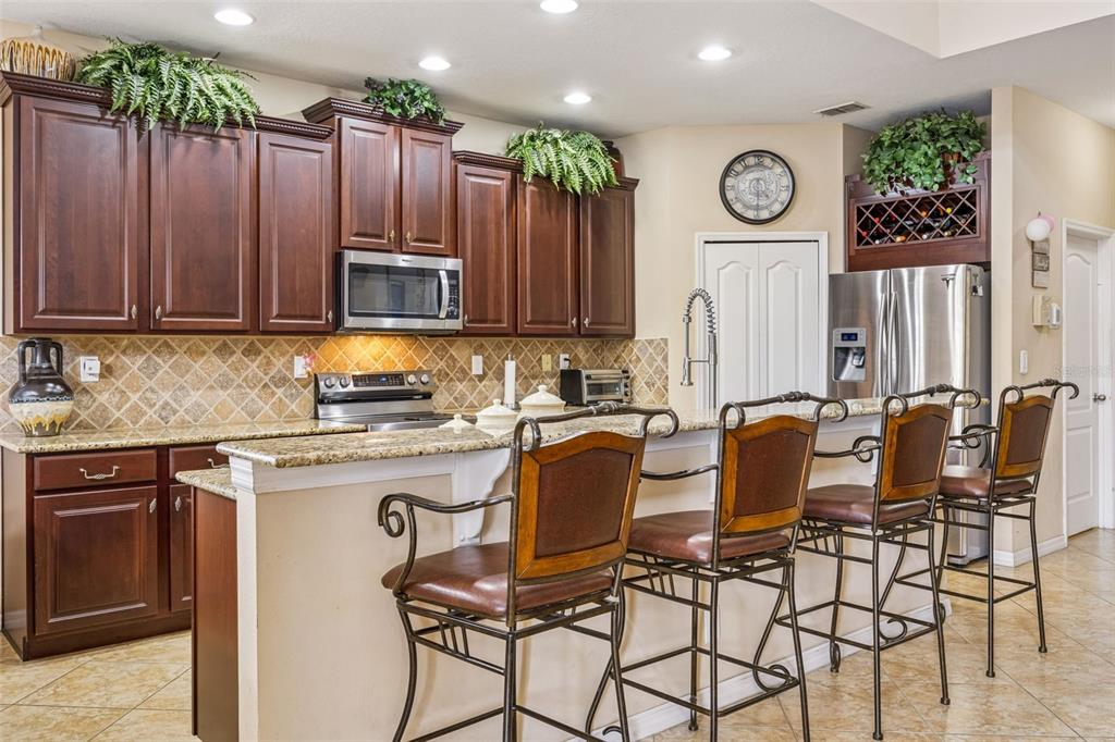 A kitchen features dark wood cabinets, granite countertops, stainless steel appliances, and three bar stools — 3676 BRIAR RUN DRIVE, CLERMONT, FL