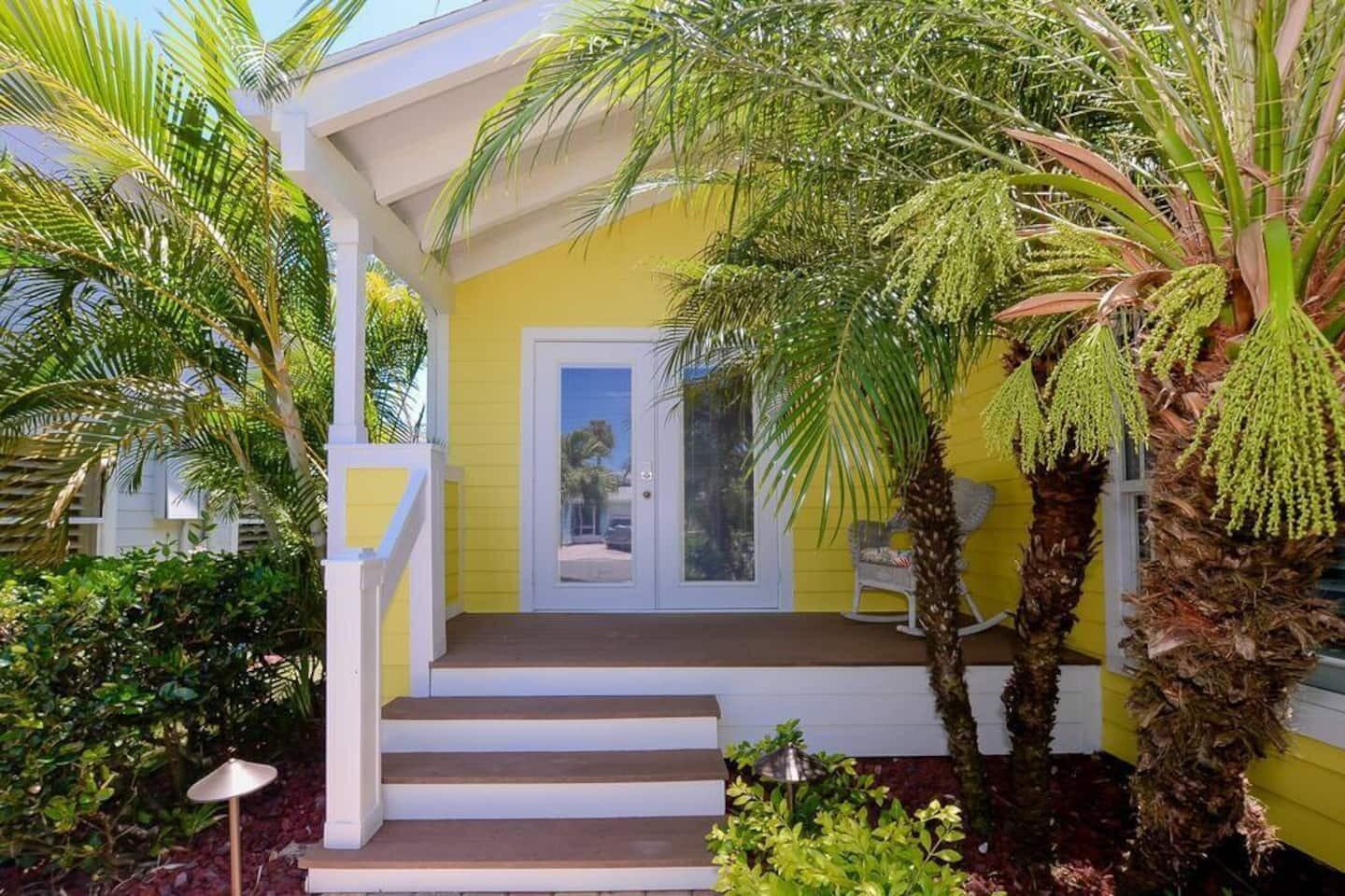 A yellow house exterior features a covered front porch with steps and a palm tree — 4031 NE Breakwater Drive, Jensen Beach FL 34957, JENSEN BEACH, FL