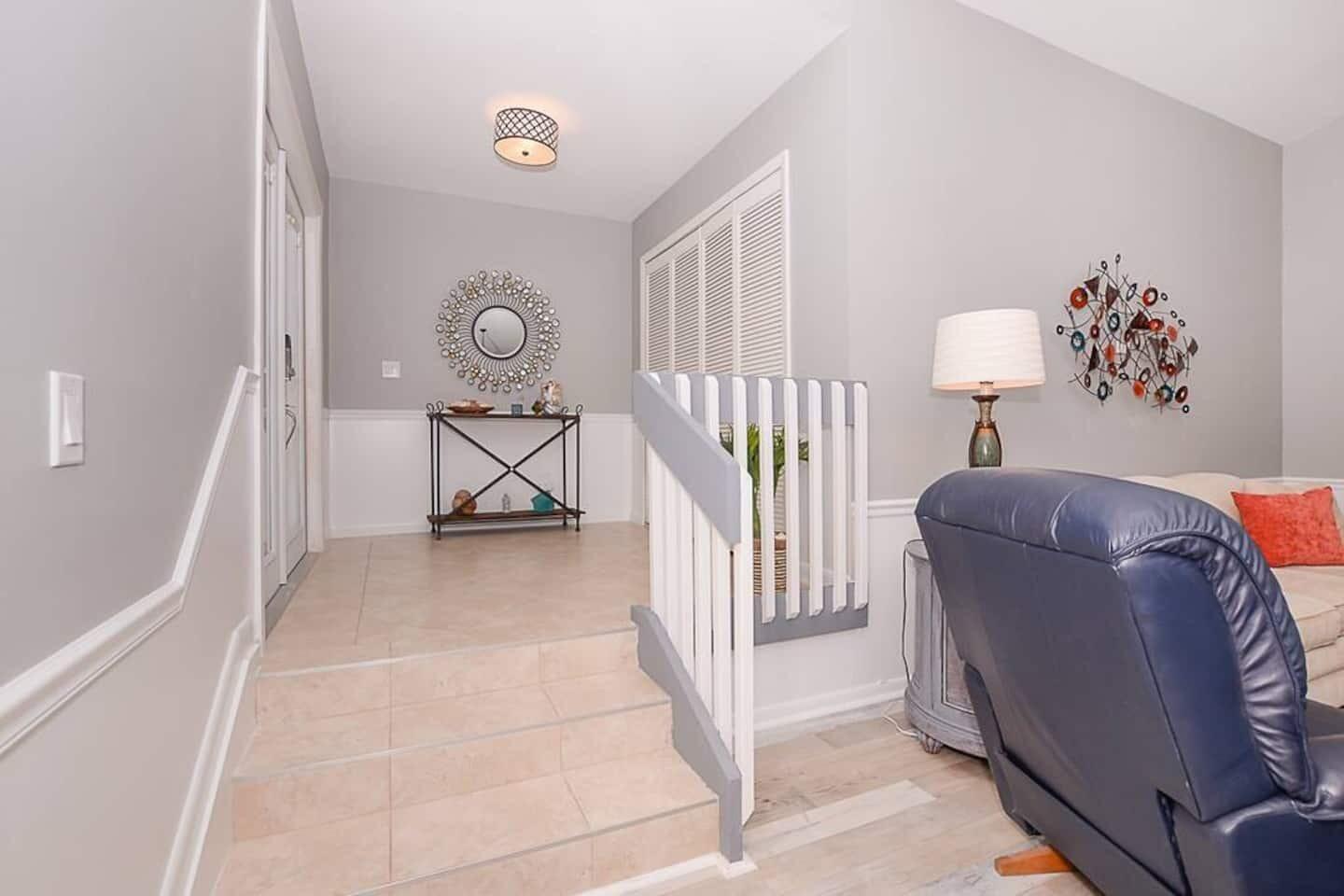 An entryway with tiled stairs leading up to a console table, mirror, and white wainscoting — 4031 NE Breakwater Drive, Jensen Beach FL 34957, JENSEN BEACH, FL