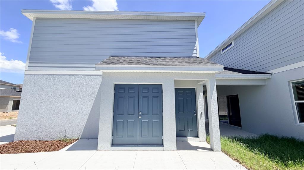 The exterior of a two-story home features blue double doors, a single door, and siding — 5694 ENCHANTED MEADOW ALLEY UNIT B, CLERMONT, FL