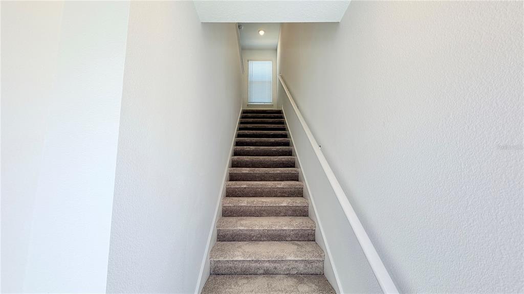 A straight staircase with gray carpet leads to a landing with a window — 5694 ENCHANTED MEADOW ALLEY UNIT B, CLERMONT, FL