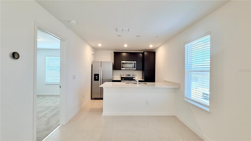 A kitchen features dark cabinets, stainless steel appliances, a white island, and light tile flooring — 5694 ENCHANTED MEADOW ALLEY UNIT B, CLERMONT, FL