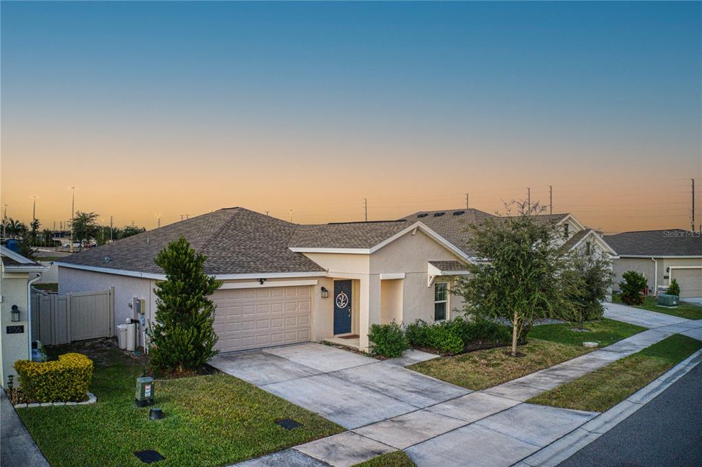 A single-story suburban house with a tan stucco exterior, a two-car garage, and a driveway — 1159 POMELO STREET, DAVENPORT, FL