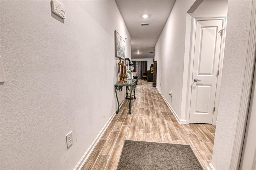 A hallway with light wood-look tile flooring leads toward a living area — 1159 POMELO STREET, DAVENPORT, FL