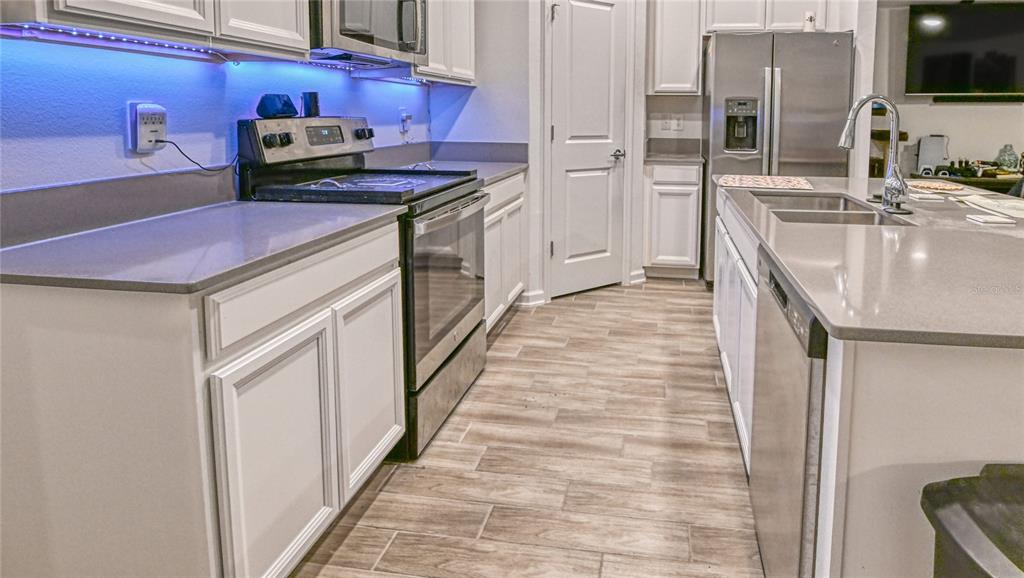 A kitchen features white cabinets, gray countertops, stainless steel appliances, and wood-look tile flooring — 1159 POMELO STREET, DAVENPORT, FL
