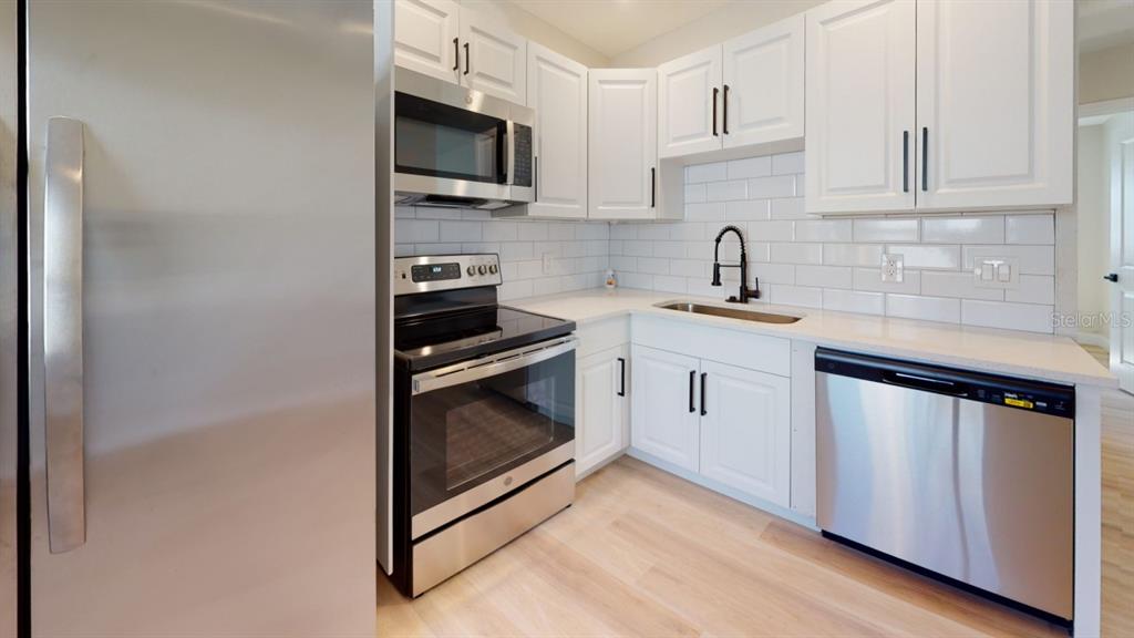 A kitchen with white cabinets, stainless steel appliances, a subway tile backsplash, and light wood flooring — 5022 10TH AVENUE N, ST PETERSBURG, FL