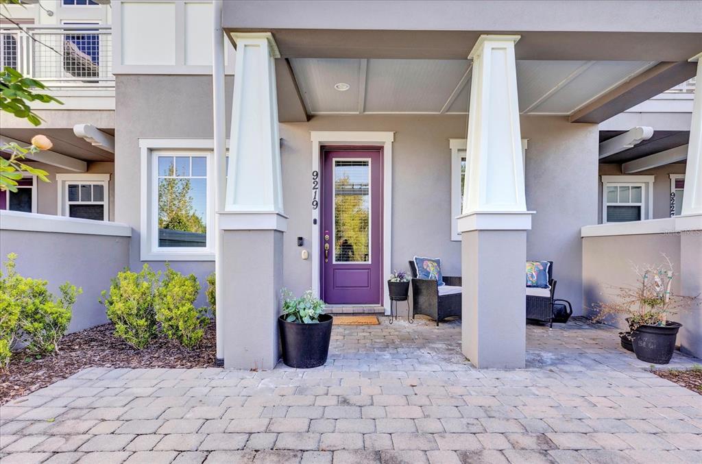 A purple front door sits under a covered porch with two white pillars and pavers — 9219 LAUREATE BOULEVARD, ORLANDO, FL